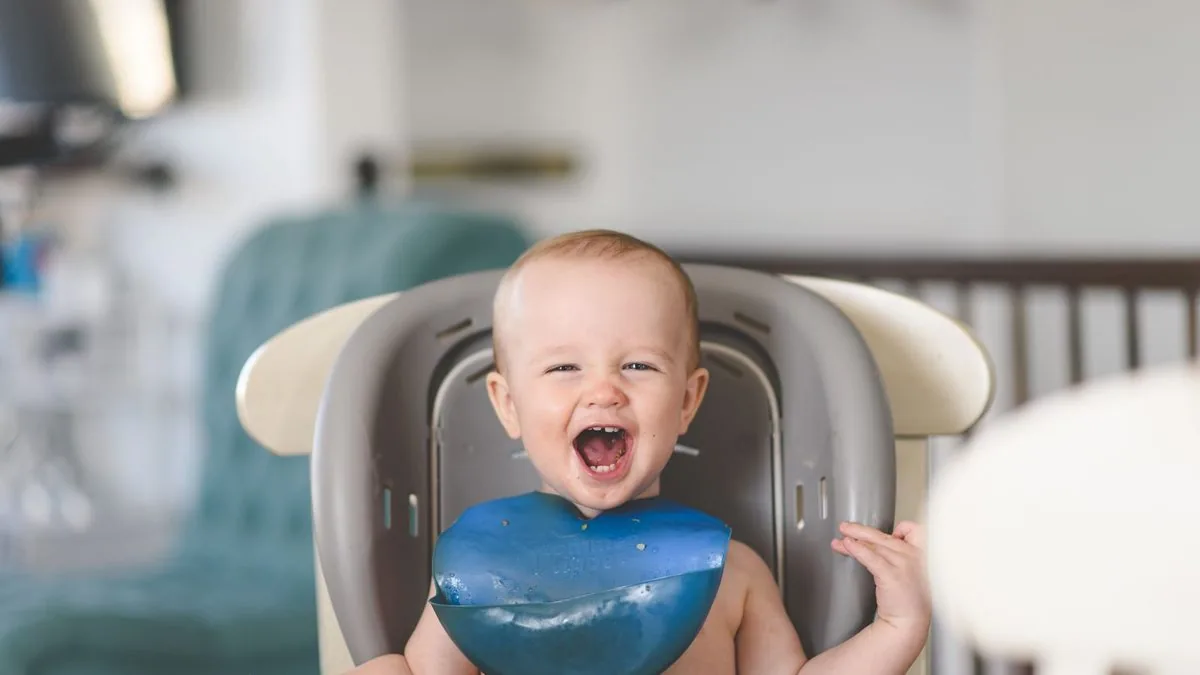 Bebê rindo na cadeira de alimentação com babador