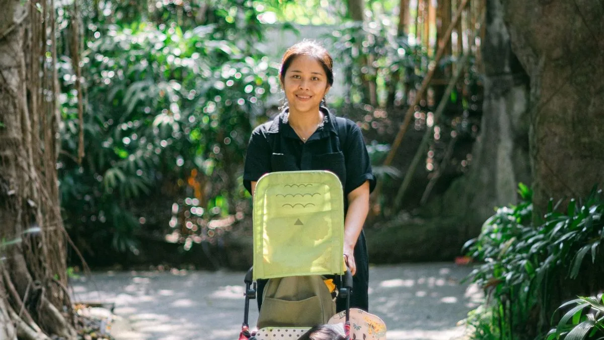 Mulher passeando com o carrinho de bebê em uma trilha arborizada