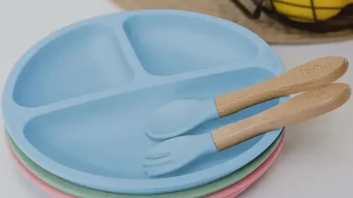 Prato de silicone azul com divisórias e ventosa ao lado de garfo e colher de madeira