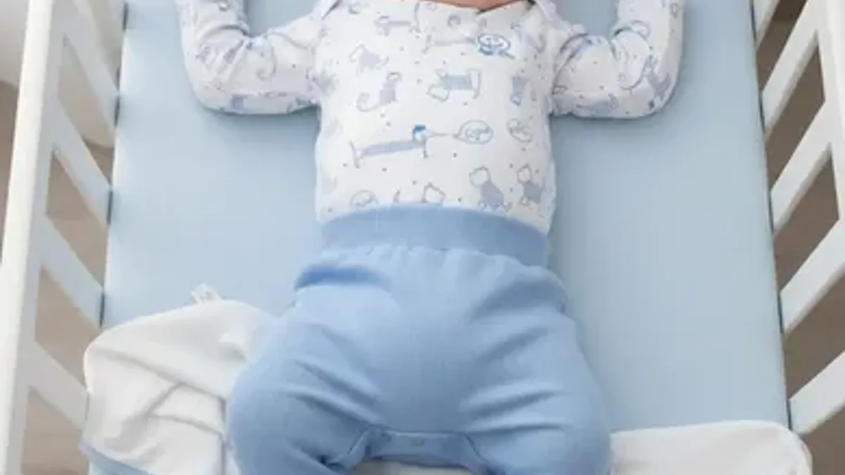 Bebê dormindo de barriga para cima no berço, de pijama de body e calça, sem cobertor