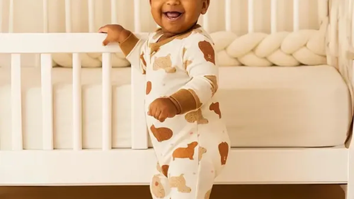 Bebê em pé ao lado do berço usando macacão pijama estampado de capivara com zíper