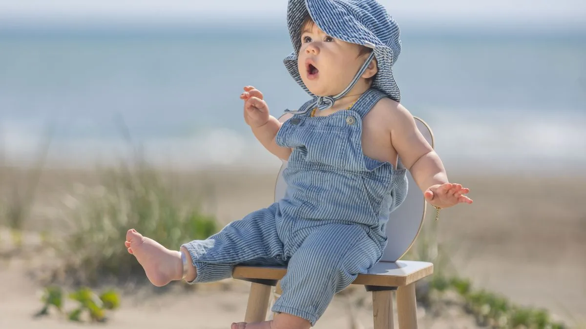 Bebê de chapéu sentado à sombra em um banquinho na praia