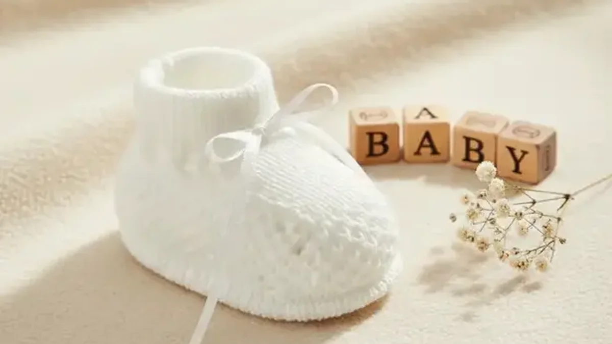 Sapatinho de tricô branco de recém-nascido sobre manta, ao lado de blocos com a palavra baby