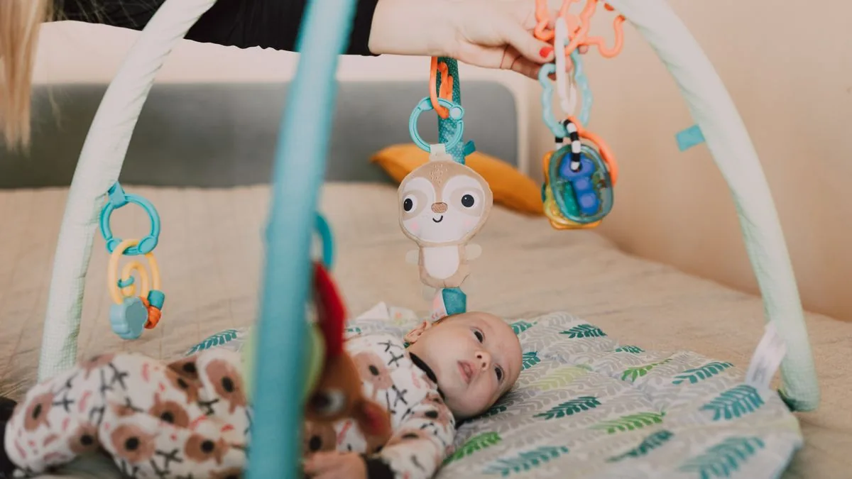 Bebê deitado de costas no tapete de atividades, alcançando os brinquedos pendurados no arco